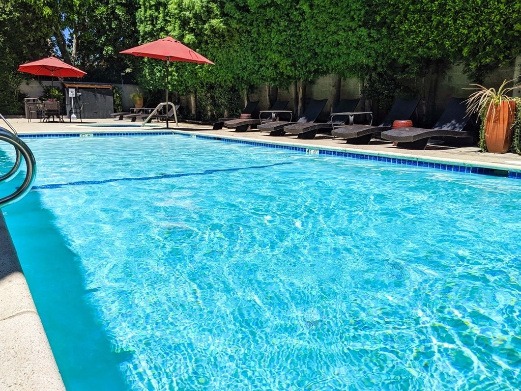 A swimming pool with red umbrellas and lounge chairs.