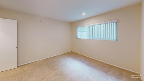 a spacious living room with a large window and beige carpet