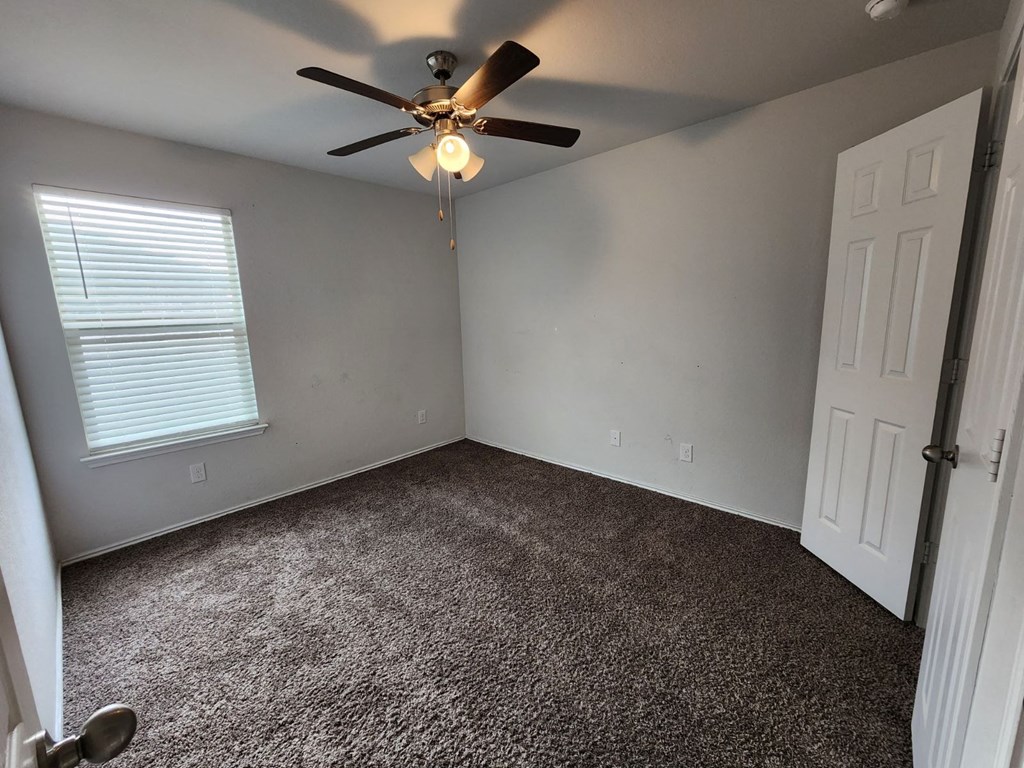 an empty bedroom with a ceiling fan and a door