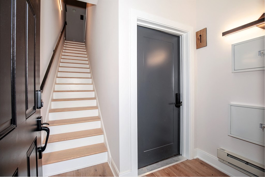 a hallway with a staircase and a black door to a room with stairs and