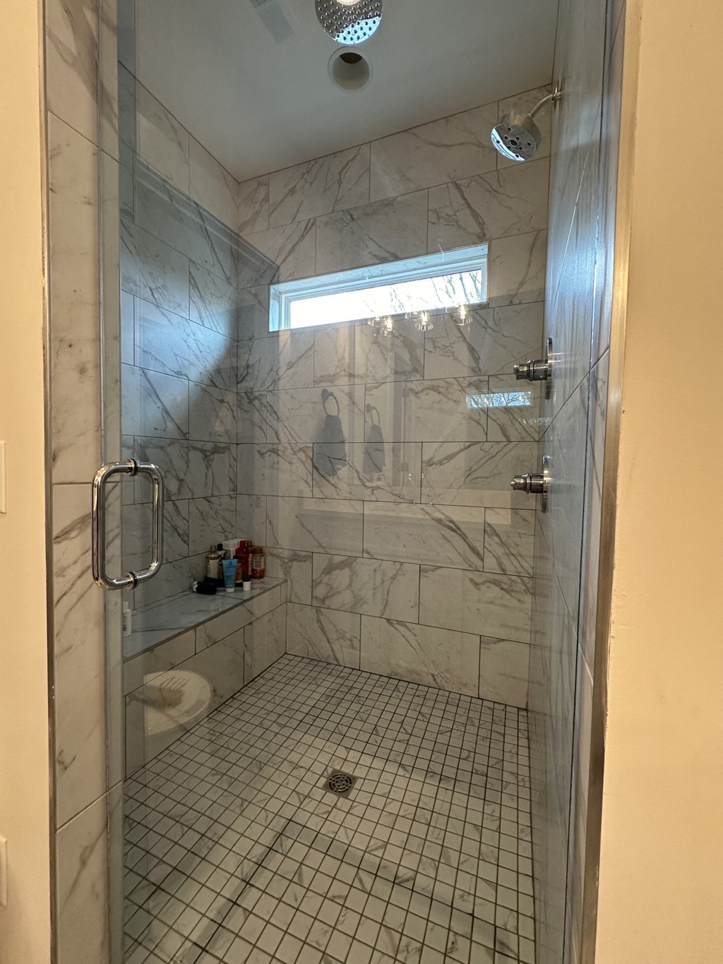 a large shower with a glass door in a white marble bathroom