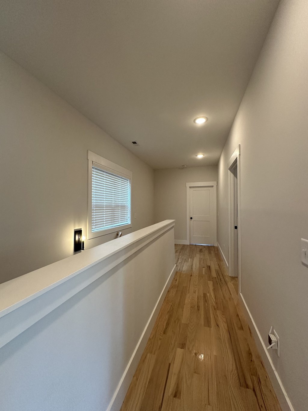 a long hallway with white walls and wood floors and a window