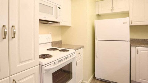 A white kitchen with a stove, microwave, and refrigerator.