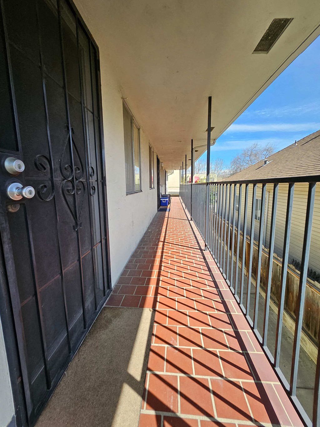 a long balcony with a black gate and a brick sidewalk