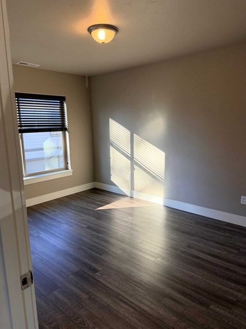 A room with wooden floors and a window with blinds.