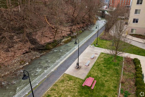 A river flows through a city park with a bench and lamp posts.