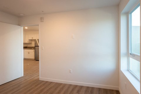 A room with white walls and wooden flooring with a doorway leading to another room.