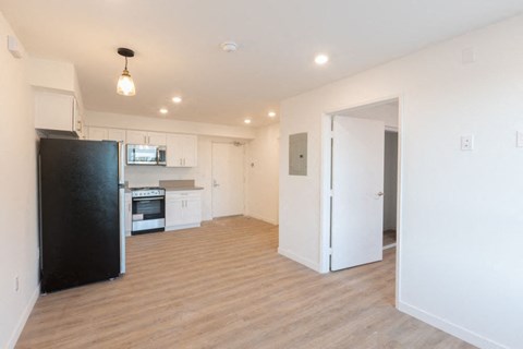 A black refrigerator is in the corner of a kitchen with white cabinets.