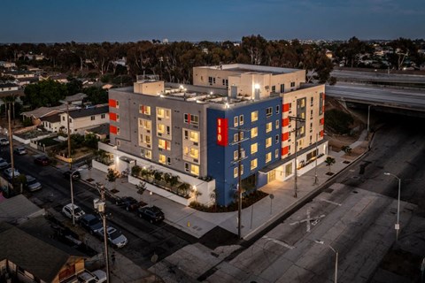 A modern multi-story building with blue and red accents is lit up at dusk.