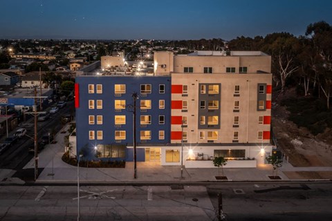 A modern building with a combination of blue, red, and beige colors is illuminated at night.