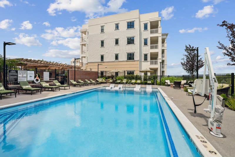 A large swimming pool in front of a building with lounge chairs around it.