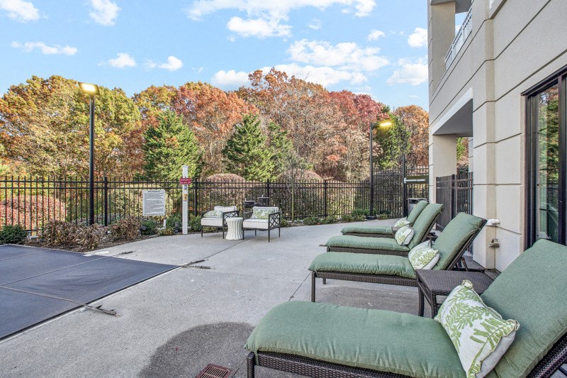 a patio with green chairs and a black fence and trees