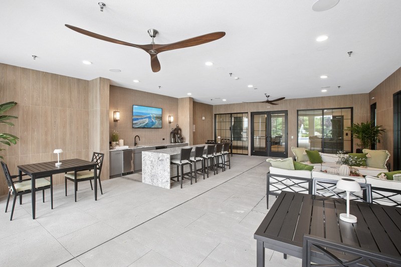 A modern outdoor dining area with a ceiling fan and a painting on the wall.