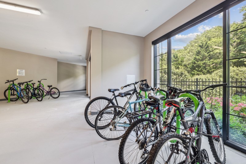A room with a white floor and a wall with a window has several bicycles parked inside.