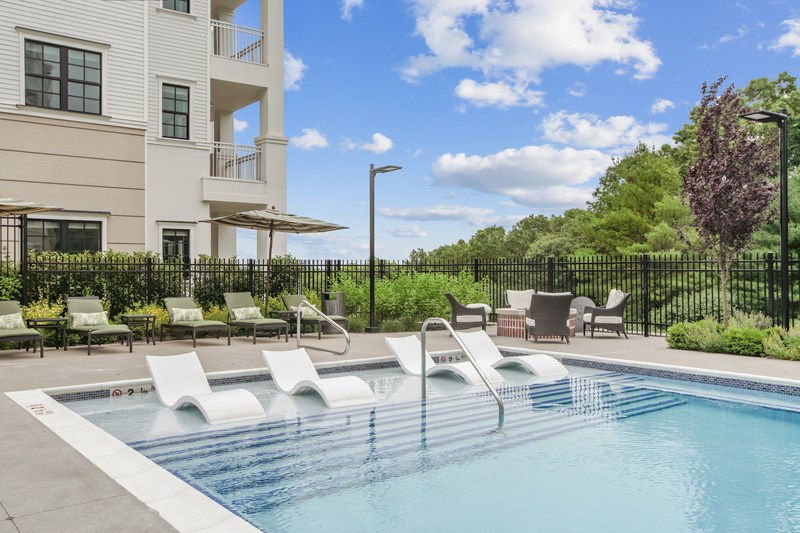 A pool with lounge chairs and a building in the background.