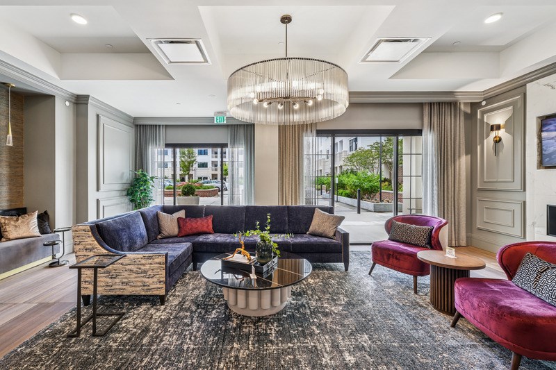 A large, modern living room with a dark rug and a large chandelier.
