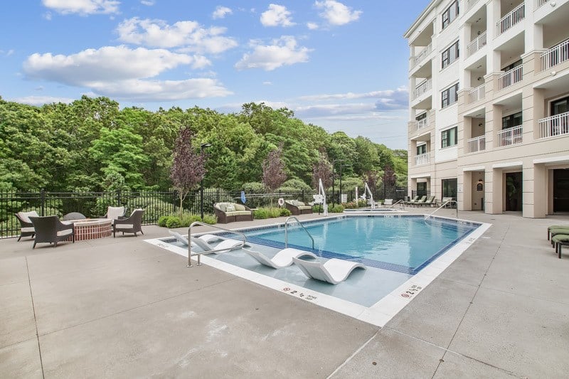 A large swimming pool surrounded by a concrete patio and a white building with balconies.