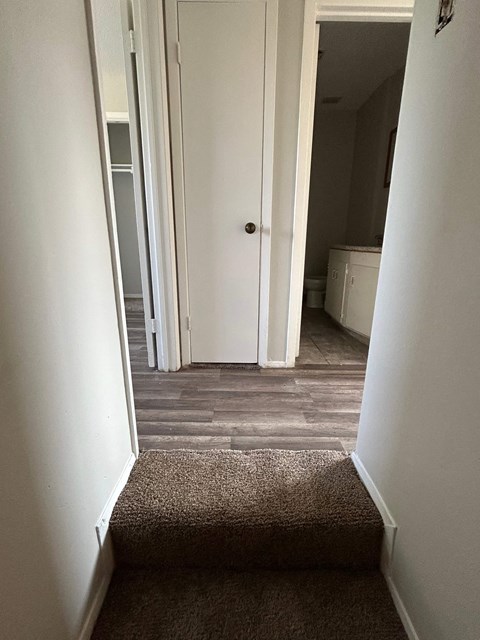 a view down the stairs of a hallway with a hallway door open to a kitchen