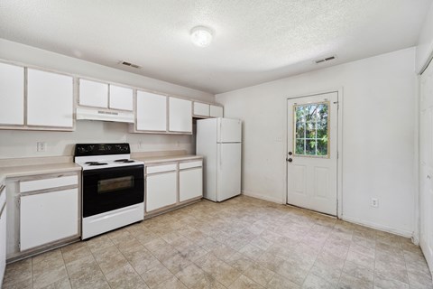 A kitchen with white cabinets and appliances, a window, and a door.