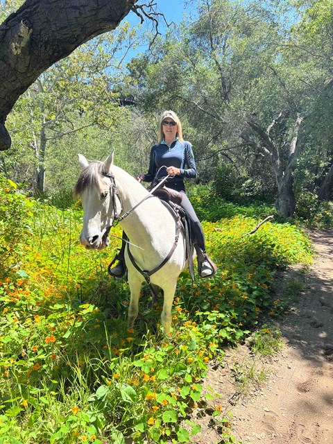 A woman riding a white horse on a trail in the woods.