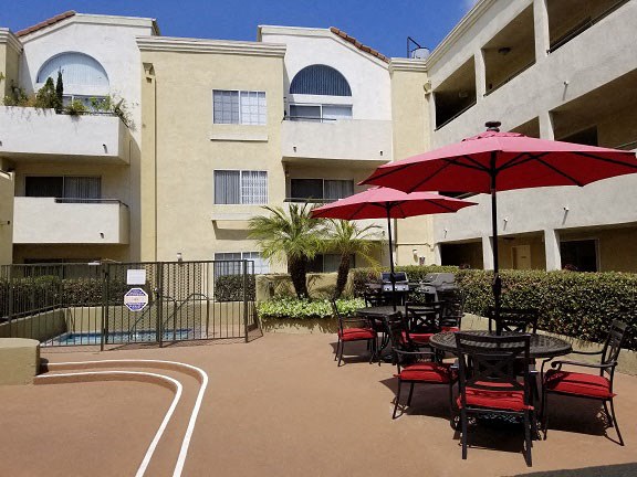 a patio with tables and umbrellas in front of an apartment building