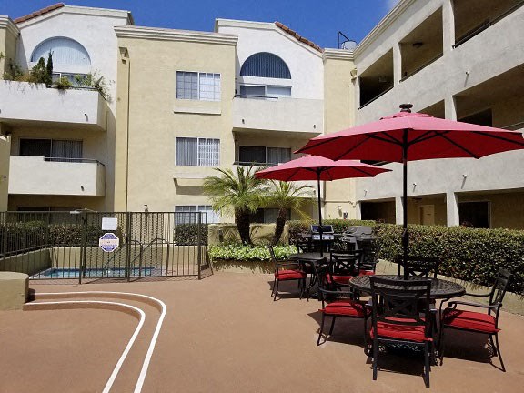 a patio with tables and umbrellas in front of an apartment building