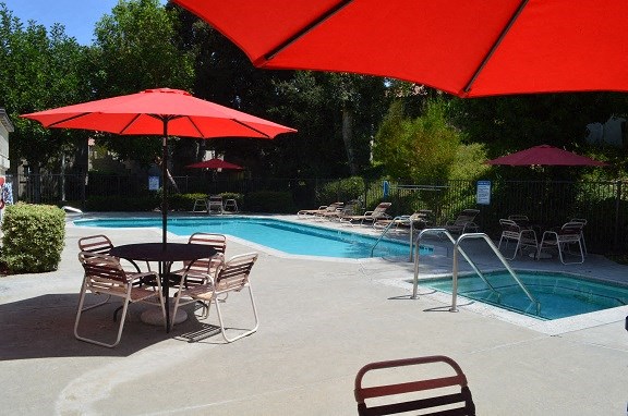 a swimming pool with tables and chairs under a red umbrella