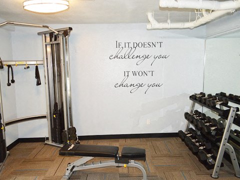 a gym with weights and a white wall with the quote if it doesnt challenge
