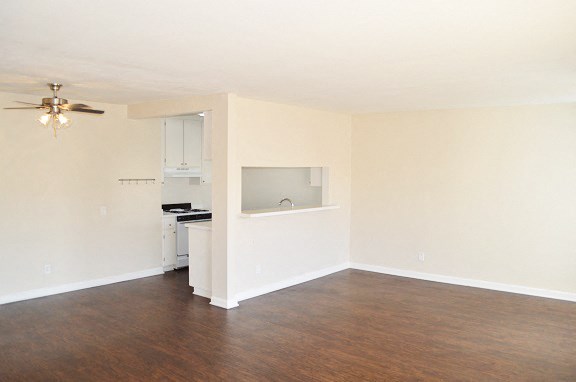 an empty living room with a kitchen and a ceiling fan
