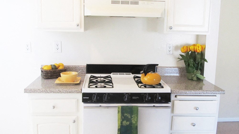 a white kitchen with a stove and a vase of yellow flowers