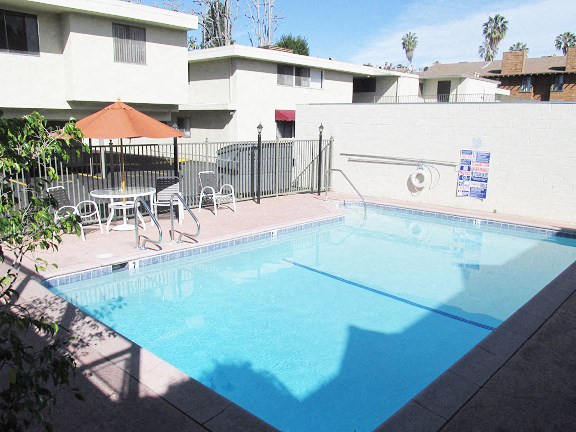 a swimming pool with chairs and an umbrella next to a fence