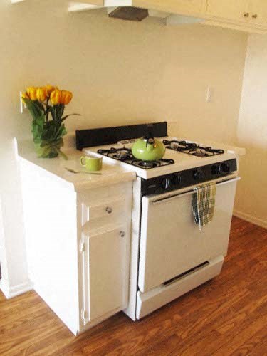 a small kitchen with a stove and a vase of flowers