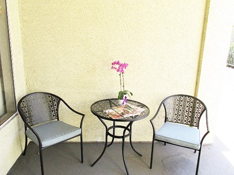 a patio with two chairs and a table with a flower on it