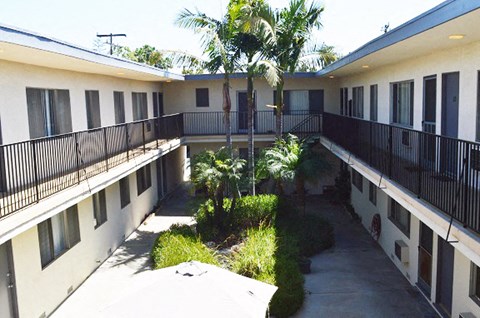 the courtyard of an apartment building with balconies and palm trees