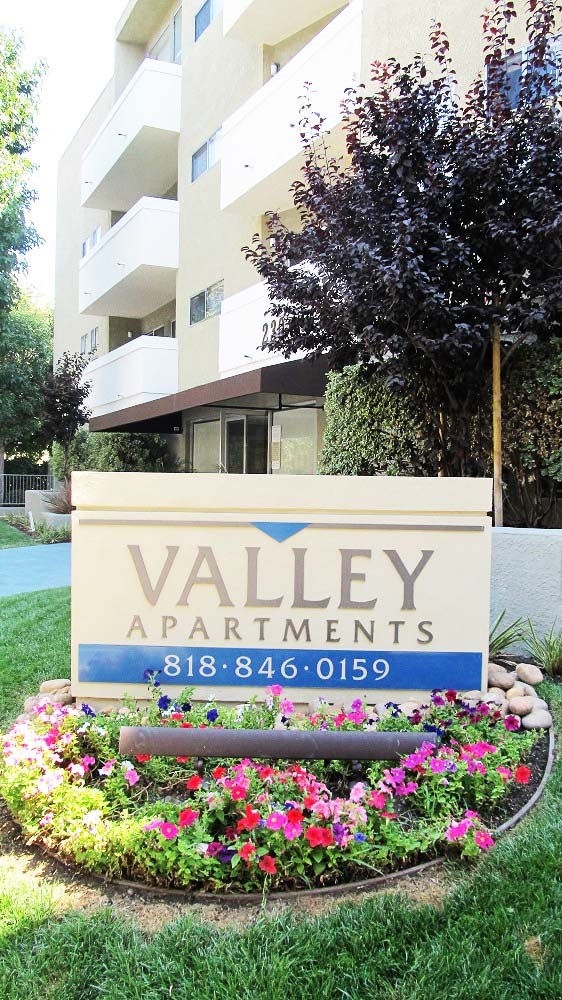 a sign forvalley apartments with flowers in front of it