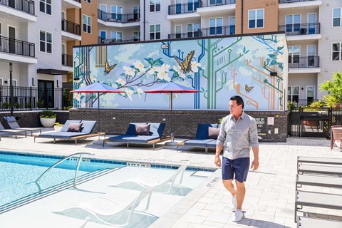 A man is walking in a pool area with a mural of a tree and birds on the wall.