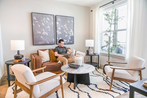 A man is sitting on a couch in a living room with a painting on the wall behind him.