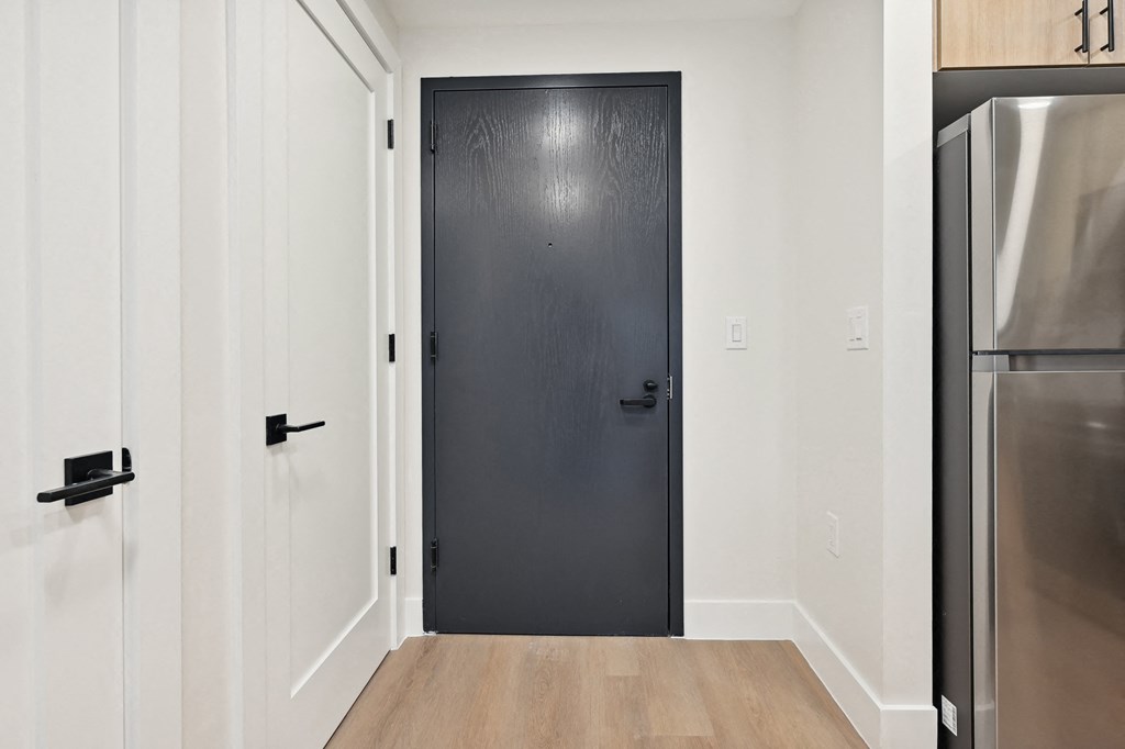 a black door in a room with white walls and a refrigerator