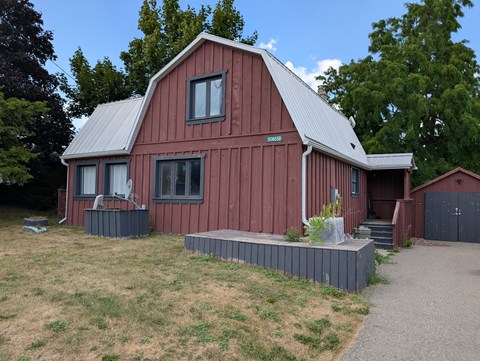 A red barn with a metal roof and a grey concrete walkway in front.