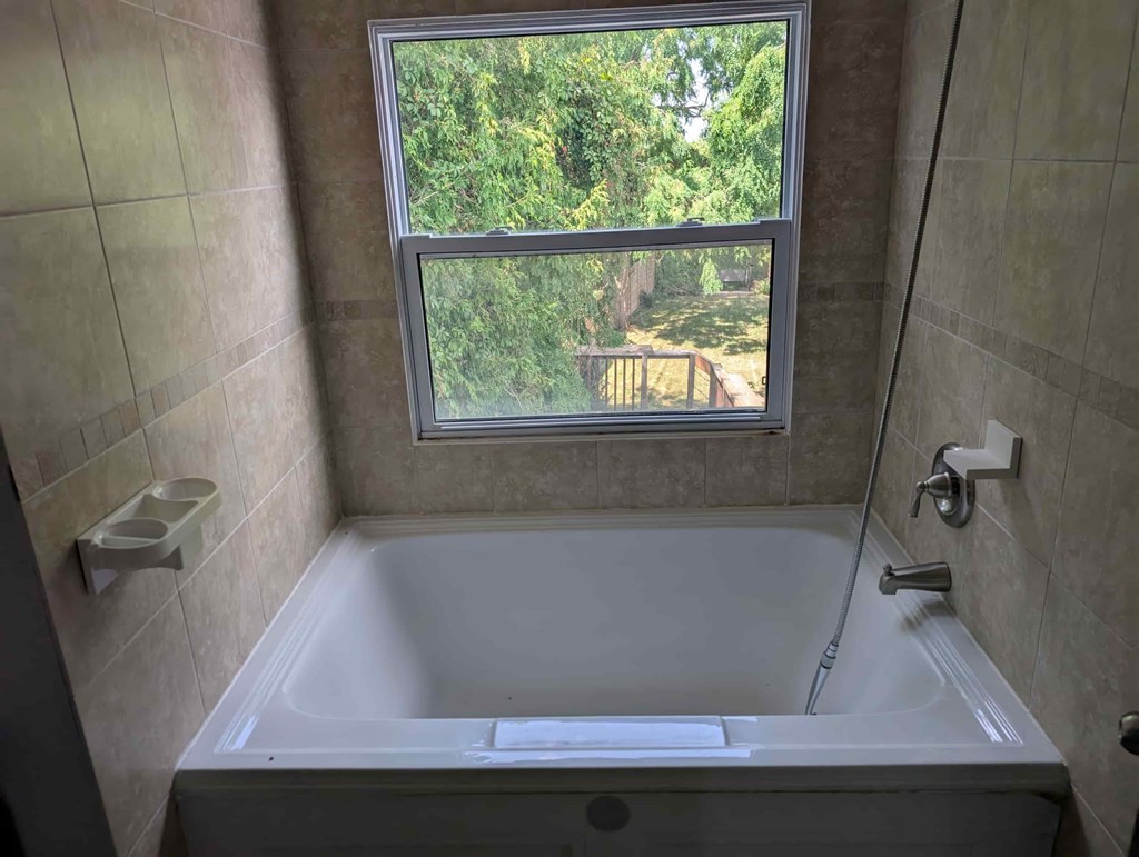 A bathroom with a tub and a window overlooking a backyard.
