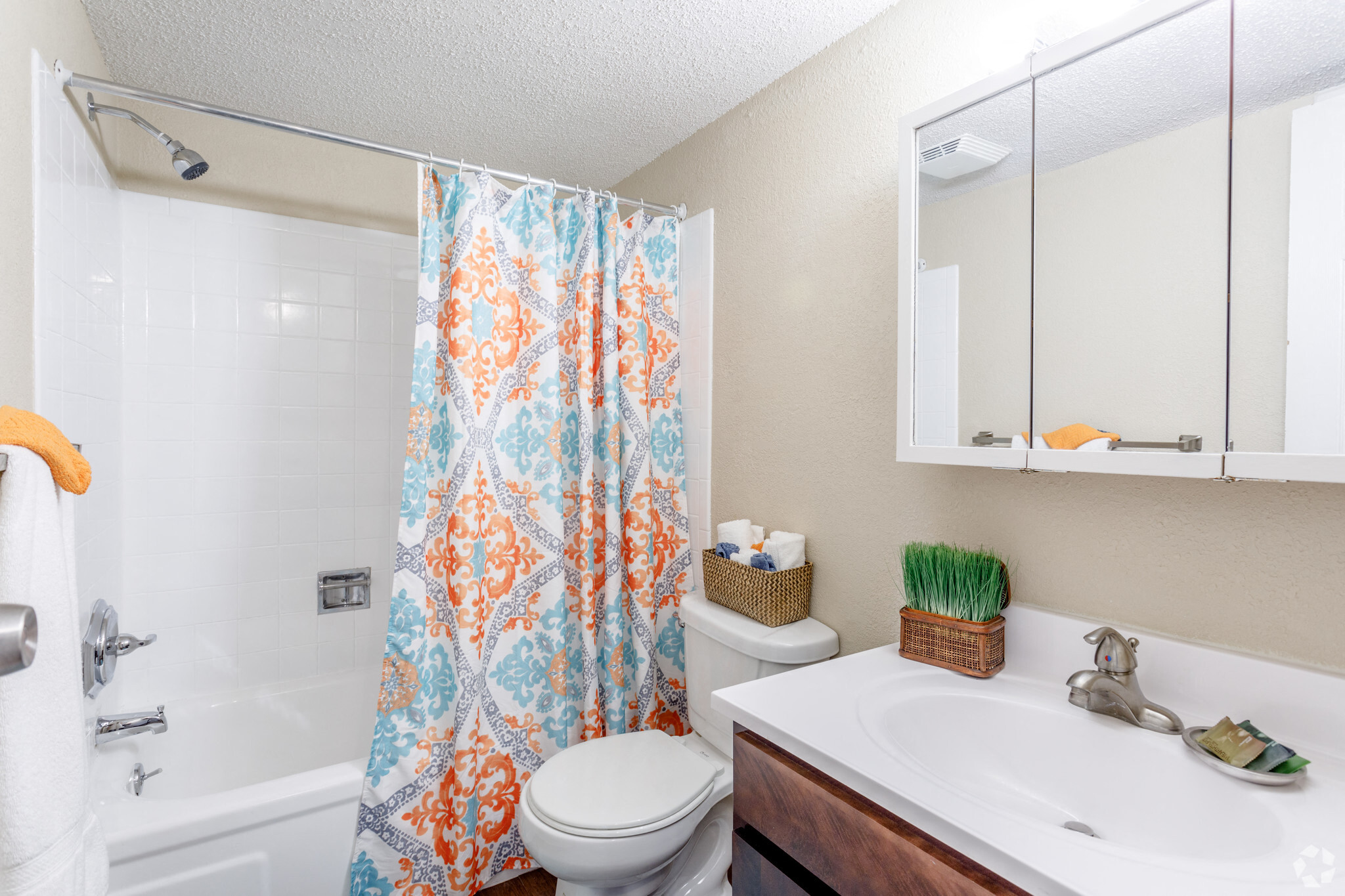 Modern bathroom with mirrored three panel medicine cabinet and tub with colorful shower curtain