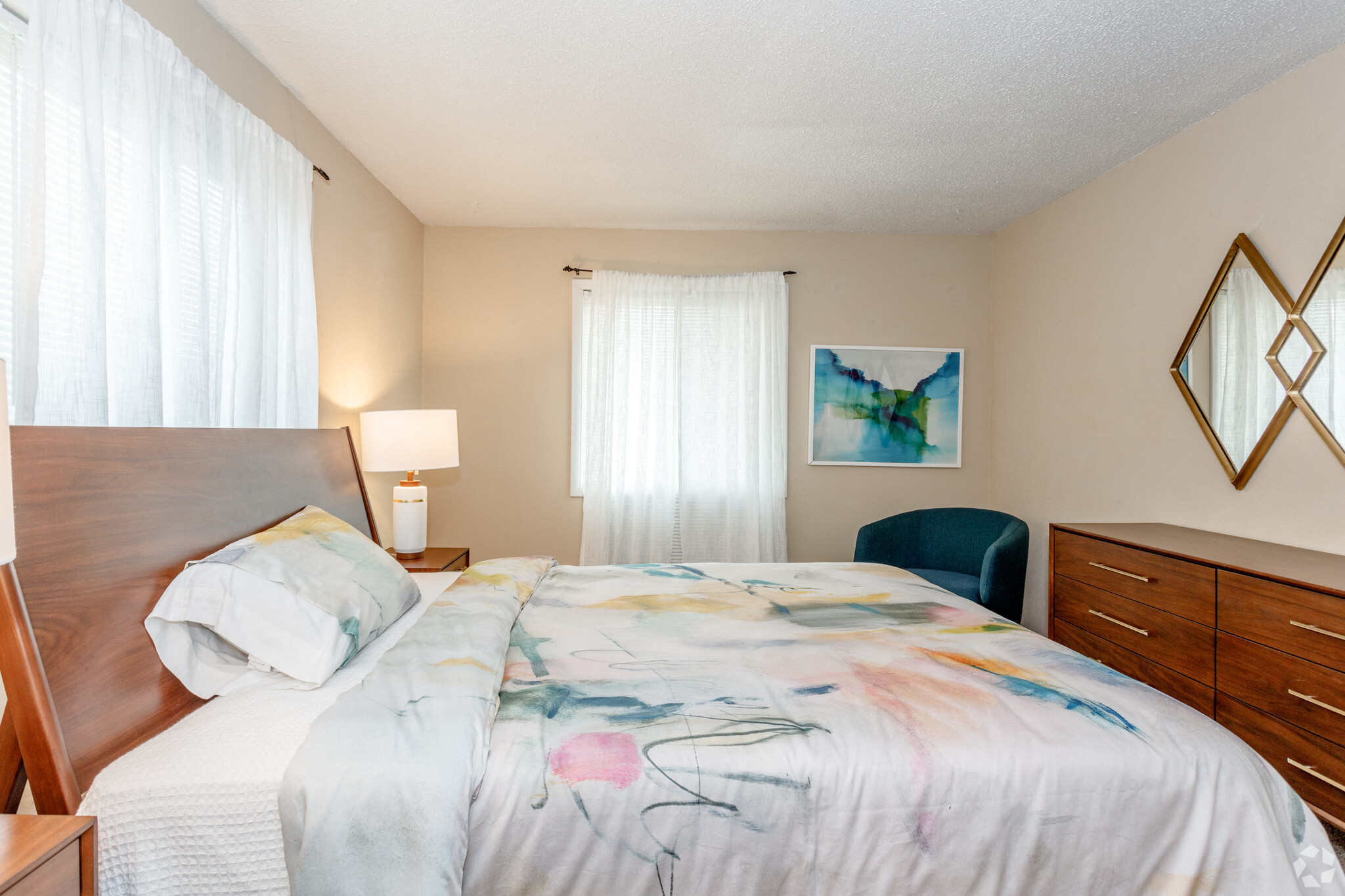 Large bed with colorful bedding and a cedar headboard and modern mirror on wall