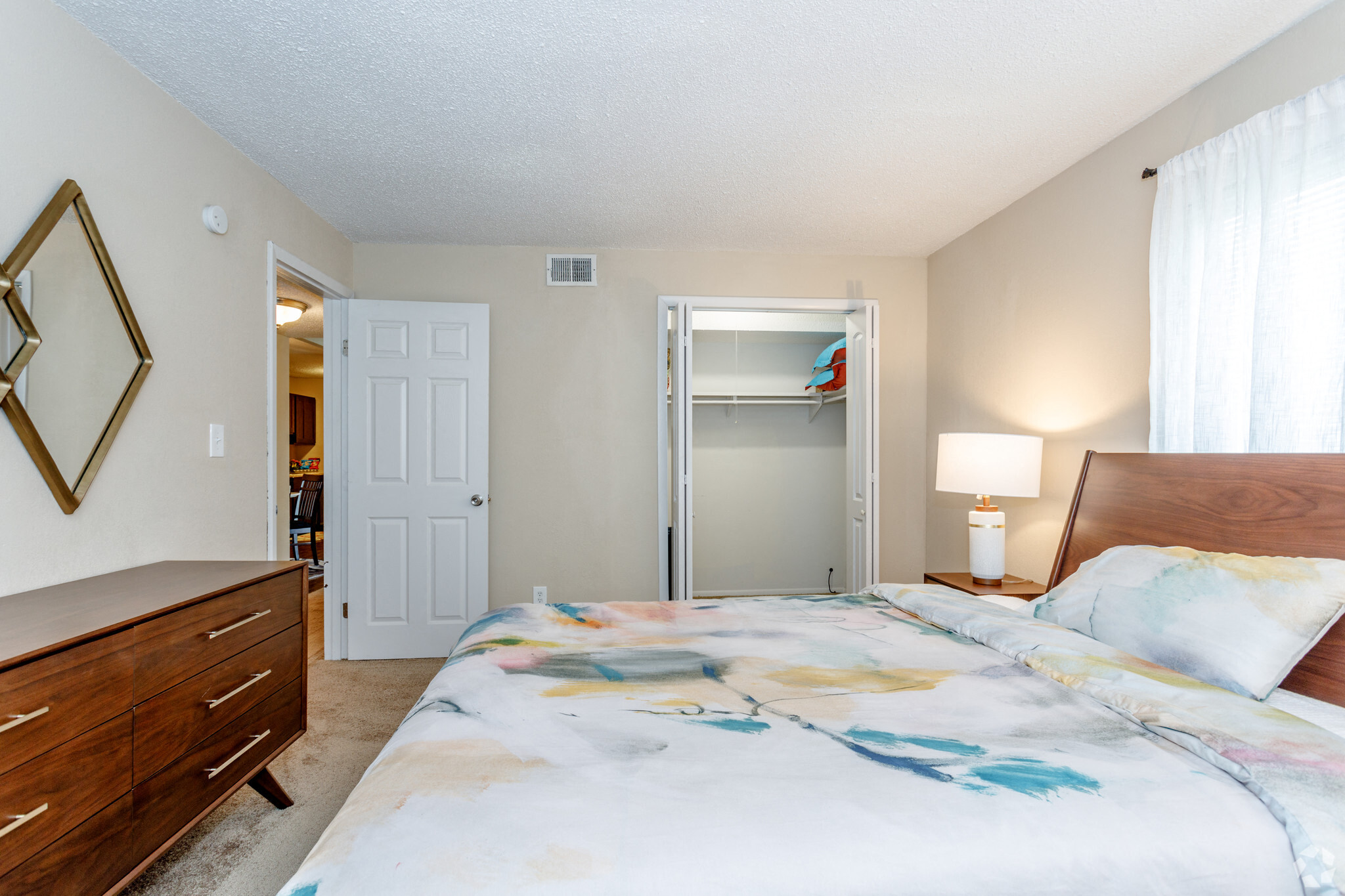 large carpeted bedroom with large two paneled closet, modern cedar dresser and large bed with colorful bedding
