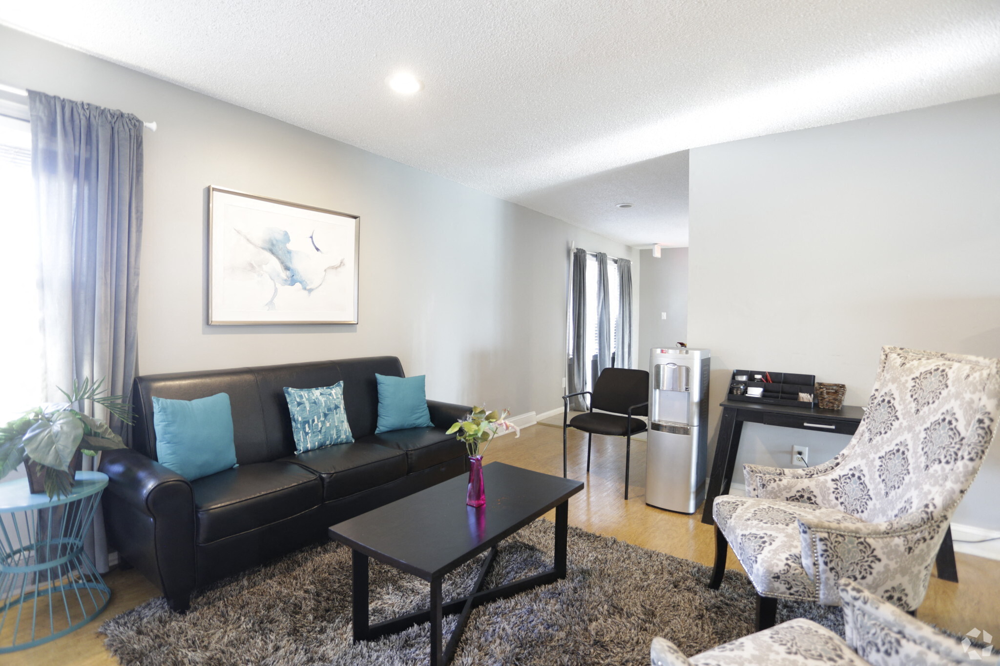 large living room with modern wood panel flooring and black sofa with paisley arm chairs