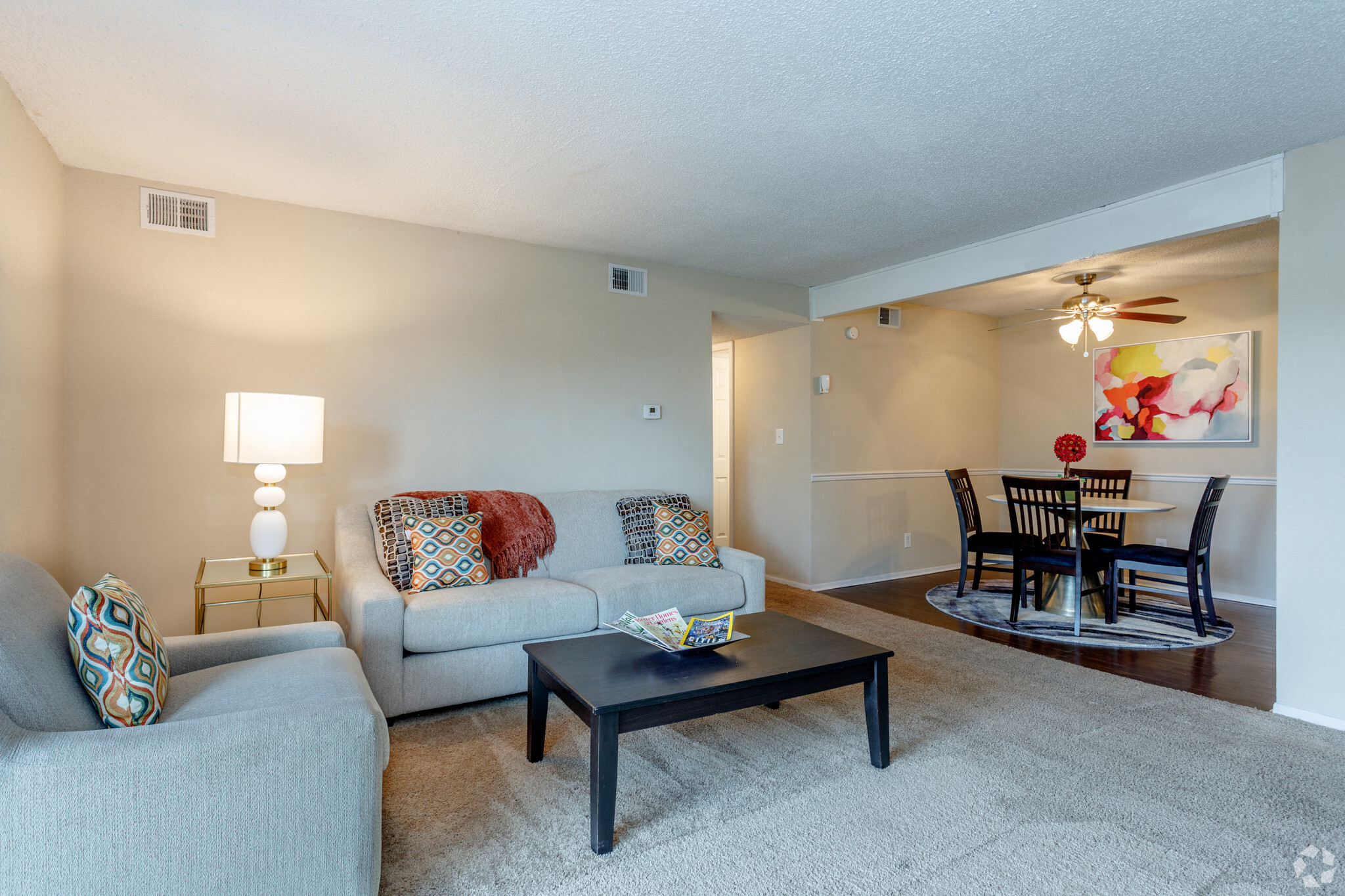 Living room with light grey carpeting and couches with a view of the dining room with dark wood panel flooring