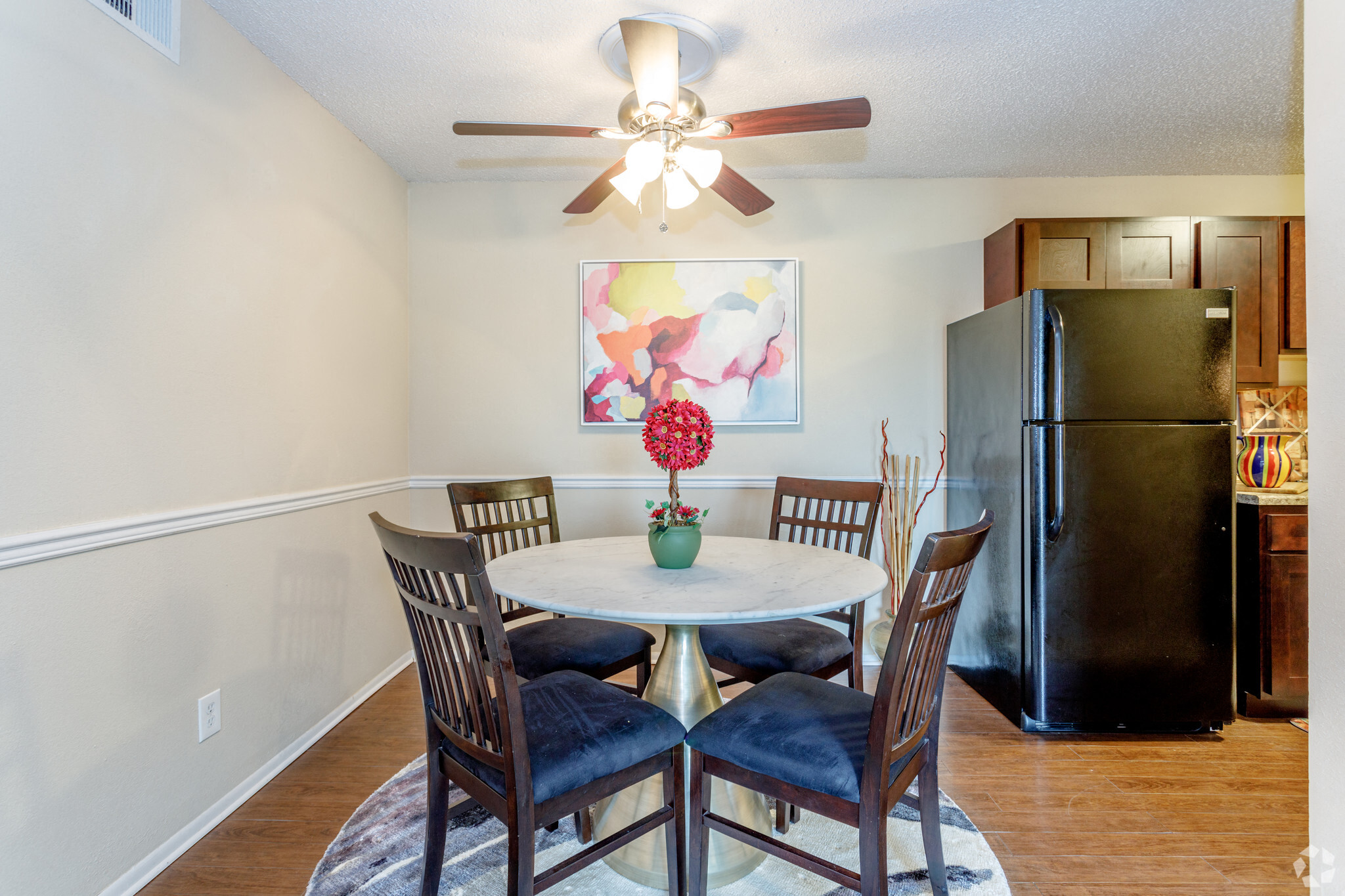 dining room with dark wood panel flooring and a round light colored table and ceiling fan and black appliances in view
