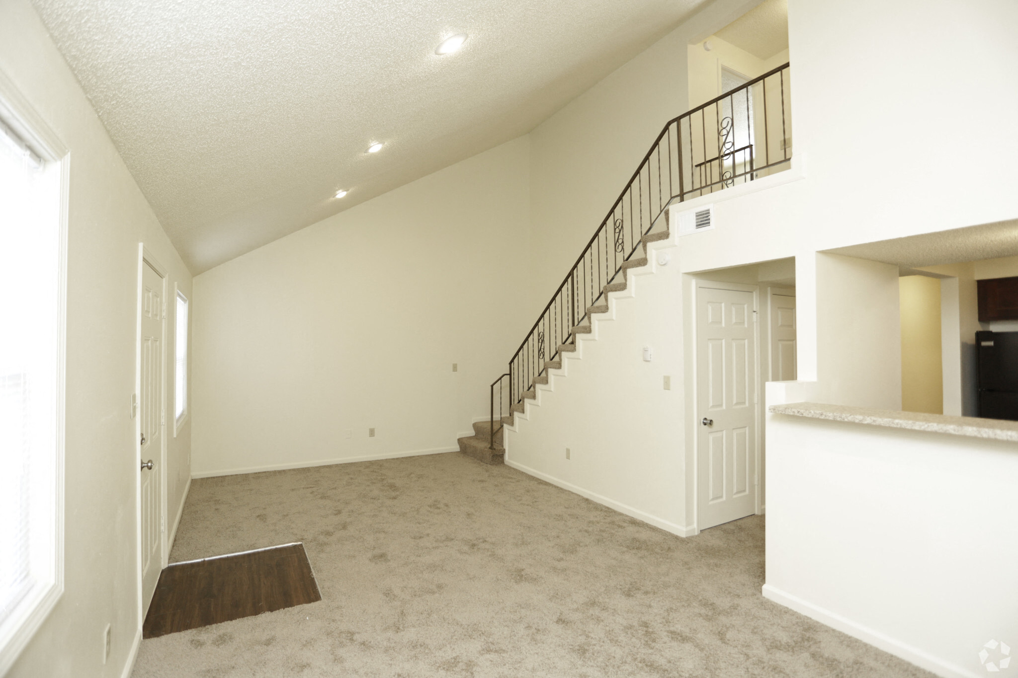 Spacious living room with white walls and gray carpeting with a view of a flight of stairs that lead to the loft