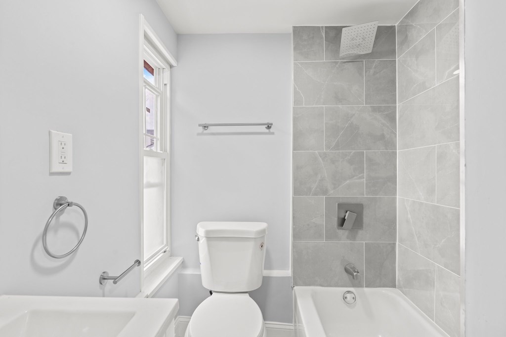 A white toilet sits in a bathroom next to a bathtub.