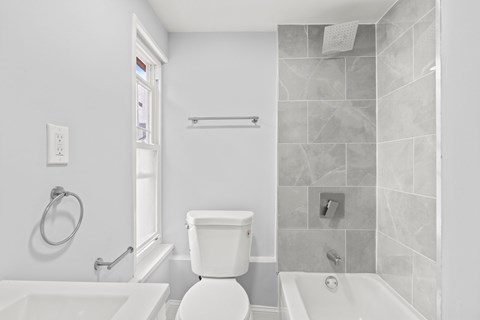 A white toilet sits in a bathroom next to a bathtub.