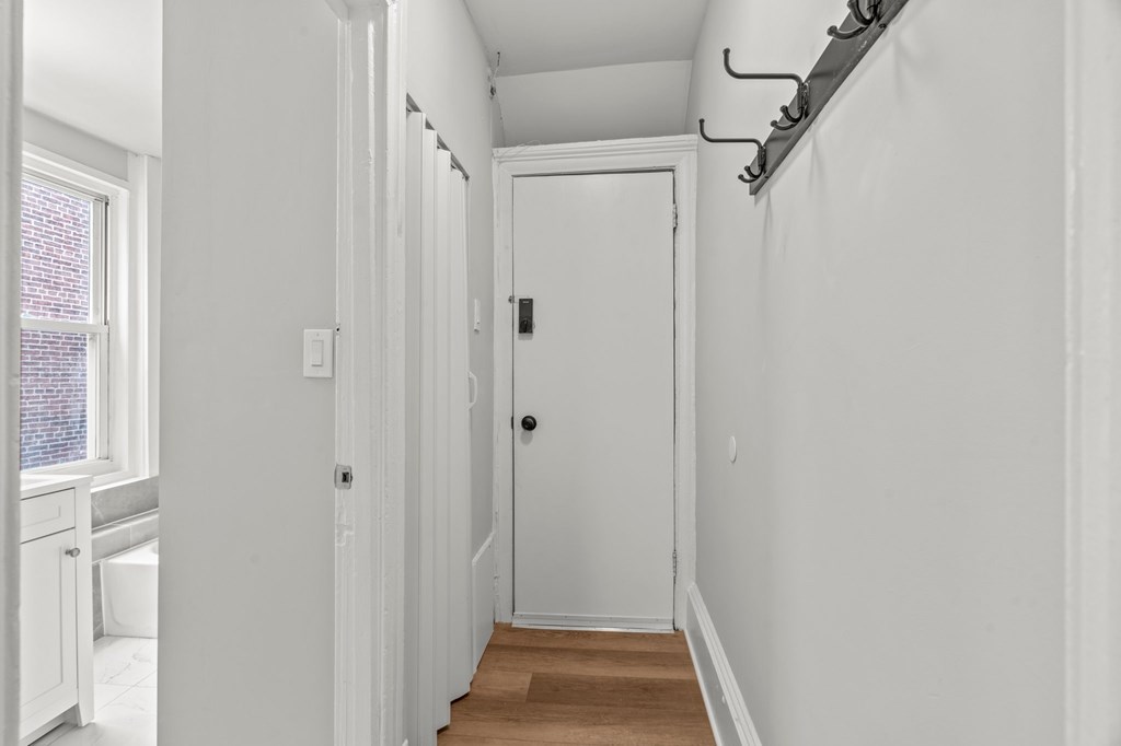 A white hallway with a door and a coat rack.